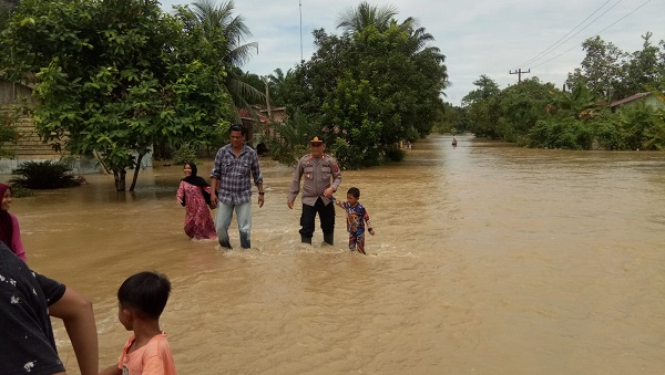 KAPOLSEK Besitang AKP Trisno Carlos Sihite bersama Kanit Intel Aiptu Leo S Surbakti mengevakuasi bocah dari arus banjir di Dusun Pantai Pulau. Waspada.id/Asrirrais