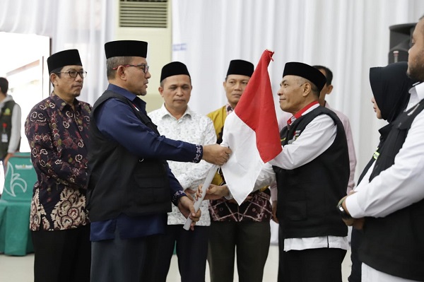 Kakanwil Kemenag Aceh yang juga Ketua PPIH Embarkasi Aceh Drs. Azhari menyerahkan Bendera Merah Putih kepada petugas saat pelepasan kloter 12 yang merupakan kloter gabungan terakhir Aceh di Asrama Haji Banda Aceh, Senin (19/06/23). (Waspada/T.Mansursyah)