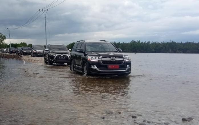 Mobil Dinas Pj Gubernur Bustami Hamzah bersama rombongan saat melintasi air pasang laut, di badan jalan Desa Kilangan menuju Desa Kayu Menang, Minggu (28/4) kemarin. WASPADA/Ariefh